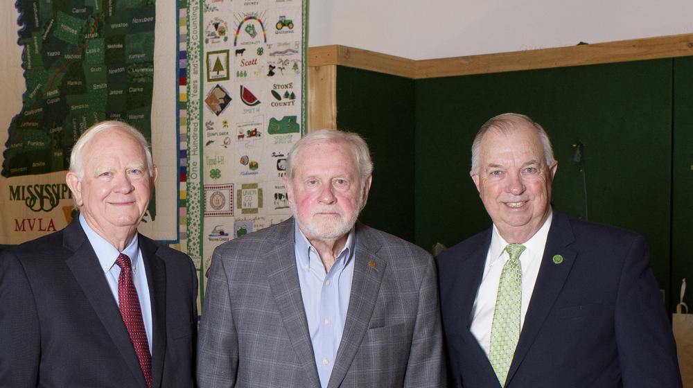 Three older men wearing suits stand next to each other.