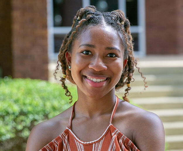 A young woman wearing a burnt orange and white striped shirt and smiling.